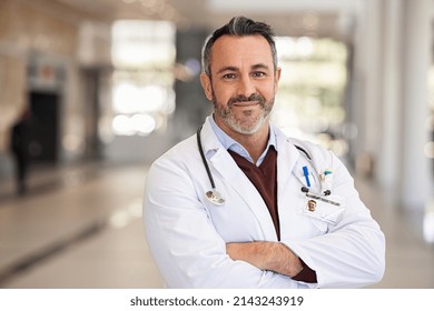 Portrait of happy doctor standing with folded hands in modern hospital corridor. Successful general practitioner looking at camera with satisfaction at private clinic. Confident proud head physician. - Shutterstock ID 2143243919