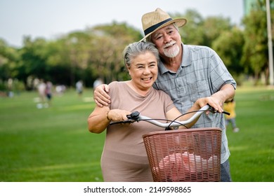 Portrait Of Happy Elderly Asian Couple Walking Talking Together With Bicycles In The Park. Holiday Activities For Retired Couples.