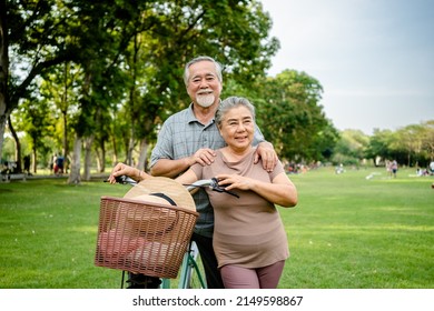Portrait Of Happy Elderly Asian Couple Walking Talking Together With Bicycles In The Park. Holiday Activities For Retired Couples.