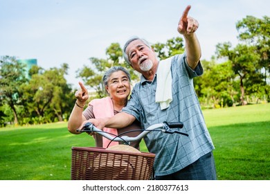 Portrait Of Happy Elderly Asian Couple Walking Talking Together With Bicycles In The Park. Holiday Activities For Retired Couples.