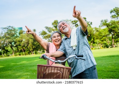 Portrait Of Happy Elderly Asian Couple Walking Talking Together With Bicycles In The Park. Holiday Activities For Retired Couples.