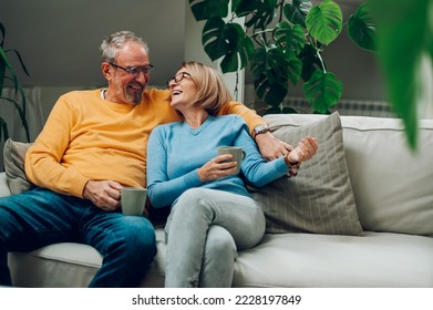 Portrait of a happy elderly couple hugging and relaxing together on the sofa at home and drinking coffee. Senior couple having a conversation together while relaxing on the couch. Copy space. - Powered by Shutterstock