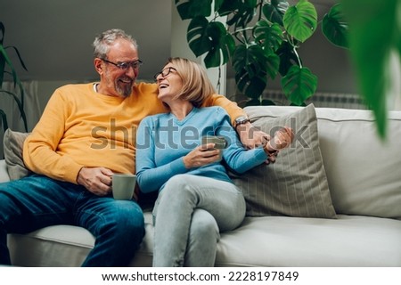 Portrait of a happy elderly couple hugging and relaxing together on the sofa at home and drinking coffee. Senior couple having a conversation together while relaxing on the couch. Copy space.