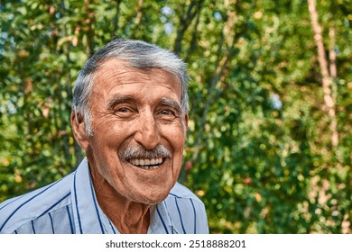 Portrait of a happy elderly man with a hearing aid, smiling warmly outdoors. His bright eyes and expressive face are surrounded by nature, reflecting joy and wisdom gained through years of life. - Powered by Shutterstock