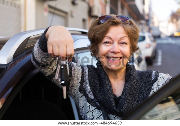 Portrait of\
happy elderly woman with keys near\
car