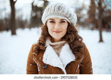 Portrait of happy elegant woman outdoors in the city park in winter in a knitted hat and sheepskin coat.