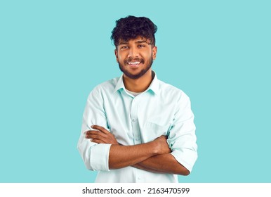 Portrait of happy ethnic student. Cheerful young dark skinned Indian, Arab, Gypsy or Bangladeshi man with curly black hair in white shirt standing with his arms folded, looking at camera and smiling - Powered by Shutterstock