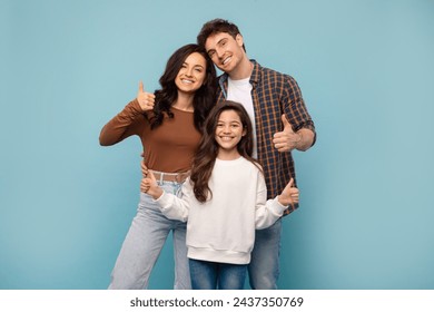 Portrait of happy european family of three showing thumbs up gesture, approving or recommending something, standing on blue studio background - Powered by Shutterstock