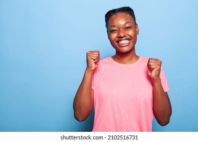 Portrait Of Happy Excited African American Young Woman Smiling At Camera While Standing In Studio With Blue Background. Concept Of Teenager Posing, Having Fun Making Joyful Facial Expression