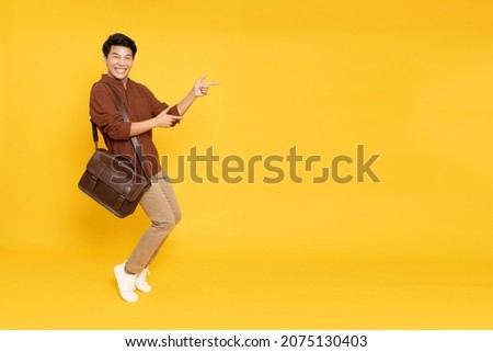 Portrait of happy excited Asian man office worker pointing hands to empty space on isolated yellow background, Full body composition and looking at camera