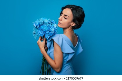 The portrait of a happy excited gorgeous young woman in an elegant blue dress is posing with a fresh bunch of blue flowers. Mothers day. Women's holidays. Springtime. Women rights