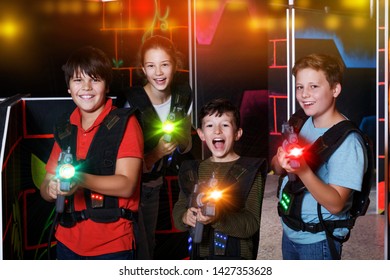 Portrait of happy excited teen kids with laser guns during lasertag game in dark room