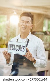 Portrait Of Happy Excited Young Coffeeshop Owner Sticking Sign On Entrance Door And Welcoming Customers Inside