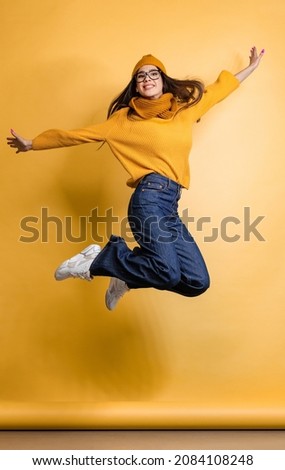Portrait of happy and excited young girl in colorful cloth jumping isolated over yellow background. Youth culture. Concept of beauty, youth, facial expression, emotions, lifestyle. Copy space for ad