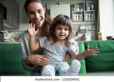 Portrait of happy excited young mother and kid girl waving hands looking at camera, smiling mom with child daughter making video call, family vloggers recording video blog or vlog together concept - Shutterstock ID 1156209061