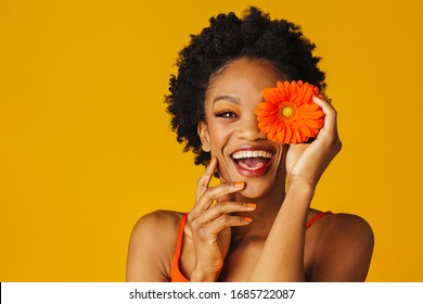 Portrait of a happy excited young woman holding orange gerbera daisy covering her eye