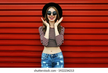 Portrait Of Happy Excited Young Woman Wearing A Black Round Hat And Sunglasses On A Red Background