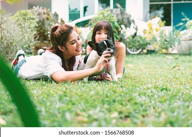 Portrait Of Happy Family In Back Yard At Home, Two Young Beautiful Women With French Bulldog Lay Down On Lawn To Play With Her Dog.