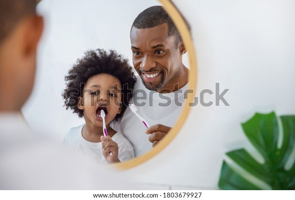 Portrait of happy family black\
African American father and son child boy brushing teeth in the\
bathroom. Morning routine with toothbrushes, father’s day\
concept