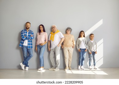Portrait of happy family consisting of three generations standing in row against gray wall. Senior parents in middle and their adult children and grandchildren on sides in casual clothes are smiling. - Shutterstock ID 2228209905