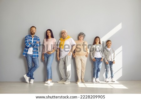 Portrait of happy family consisting of three generations standing in row against gray wall. Senior parents in middle and their adult children and grandchildren on sides in casual clothes are smiling.