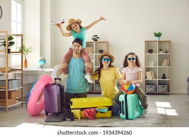 Portrait of happy family with daughters looking at camera ready to fly to tropical resort. Father and mother with little girls children having fun at home sitting on home floor next to travel luggage