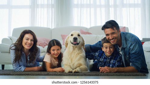 Portrait Of Happy Family With A Dog Having Fun Lying On The Carpet In Living Room. Concept Of Happy Family, Love For Animals, Pedigree Pet