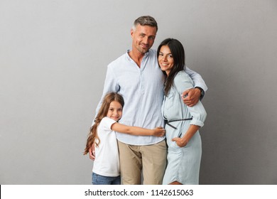Portrait of a happy family father, mother, little daughter hugging isolated over gray background