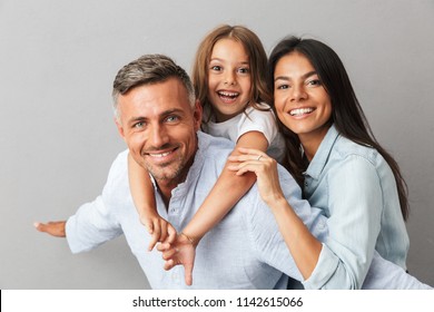 Portrait of a happy family father, mother, little daughter having fun together, father holding little daughter on his back isolated over gray background