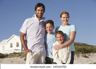 Portrait Of Happy Family Of Four With Beach House In Background