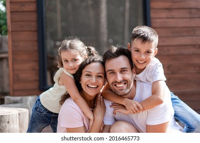 Portrait Of A Happy Family Of Four, Mom, Dad, Daughter And Son, Children Hug Parents, All Rejoice In A Joint Vacation During The Hot Summer.