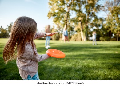 Portrait of happy family of four playing with disc on a green meadow with grass. Focus on daughter. Family, kids and nature concept. Horizontal shot. Rear view