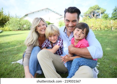 Portrait Of Happy Family Of Four Sitting In Yard