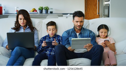 Portrait Of Happy Family Having Fun Using Different Modern Media Devices On Sofa In Living Room In Slow Motion. Concept Of  Family Entertainment, Education, Technology