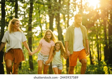 Portrait of a happy family holding hands and hiking in forest while exploring wilderness. An adventurous family is exploring forest while holding hands and taking a walk in nature. Family in woods. - Powered by Shutterstock