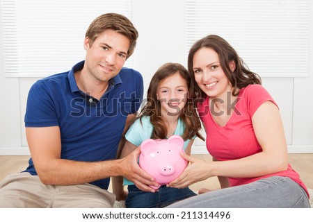 Portrait of happy family holding piggy bank while sitting on floor at home