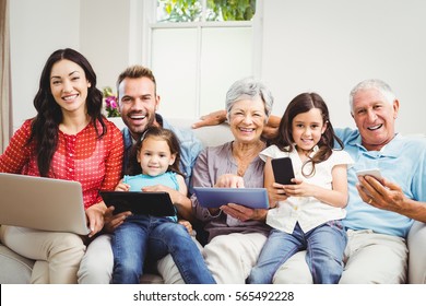 Portrait of happy family holding technologies while sitting on couch at home - Powered by Shutterstock