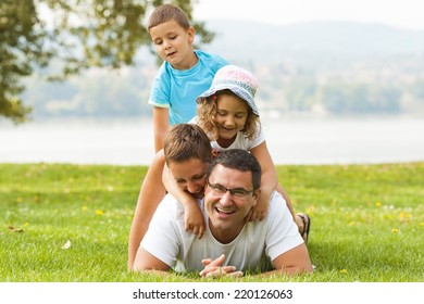 Portrait Of Happy Family Making A Human Pyramid In The Meadow. 