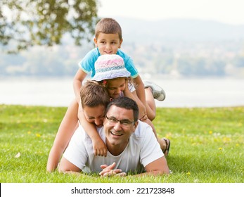 Portrait Of Happy Family Making A Human Pyramid In The Meadow. 