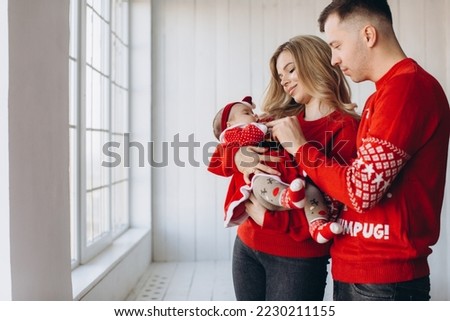 Portrait of happy family mom dad and little daughter in red traditional christmas clothes spending time together in light wooden room near window, copy space