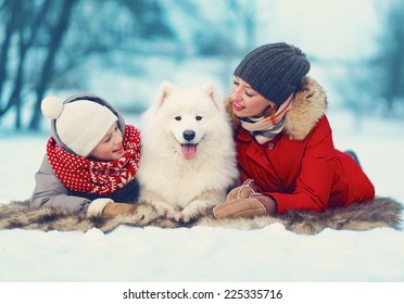 Portrait Happy Family, Mother And Son Child Walking With White Samoyed Dog Lying On Snow In Winter Day