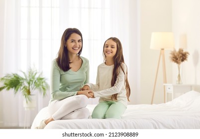 Portrait of happy family on bed at home. Smiling mother and child in comfy milk white and mint green cotton pyjamas or homewear sitting together on comfortable big bed in modern cozy bedroom interior
