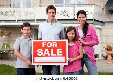 Portrait Of Happy Family Selling Their Home Holding For Sale Sign Board