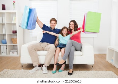 Portrait Of Happy Family With Shopping Bags Relaxing On Sofa At Home