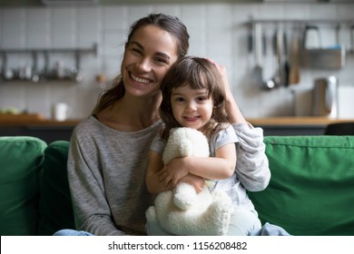 Portrait Of Happy Family Single Mother And Kid Daughter Embracing On Sofa At Home, Young Cheerful Mom Sister Stroking Cute Girl Hugging Looking At Camera, Mum And Child Sincere Relationship Concept