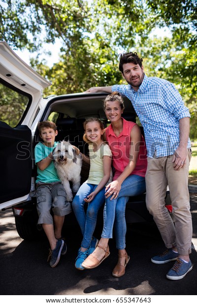 Portrait of happy family sitting in car trunk with\
their dog