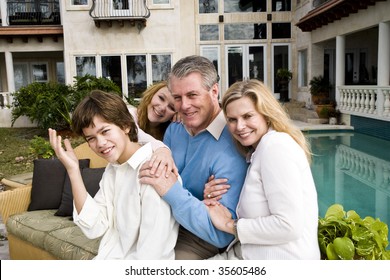 Portrait Of Happy Family Sitting Poolside On Patio