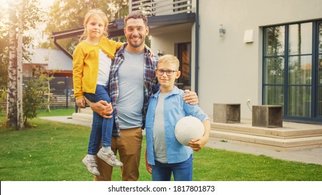 Portrait of a Happy Family of Three: Father, Daughter, Son. They Are Posing In Front of Camera on a Lawn Next to Their Country House and Smile. Dad is Holding the Girl in His Arms, Boy - Football.