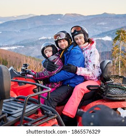 Portrait Of Happy Family Of Three, Wearing Colorful Ski Suits, Spending Great Winter Holiday, Hugging Together In Snowy Mountains On Red Quad Bike, Side View, Ridge Of Mountains On Background