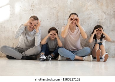 Portrait of happy family with two cute children making funny faces. Smiling parents of mother and father with daughter and son looking at camera at home, making binoculars with their fingers.